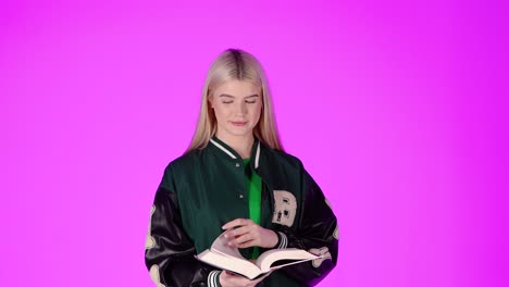 portrait of young blonde student reading a book and turning pages, colorful studio shot