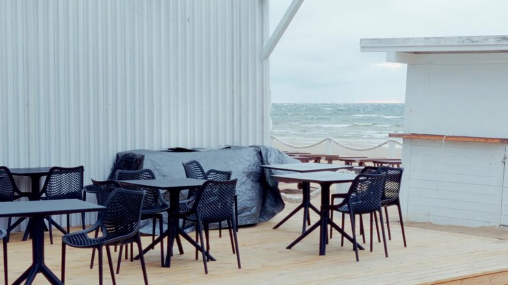 Vista a livello degli occhi di una terrazza esterna deserta di un ristorante, con moderne sedie e tavoli in plastica, affacciata sul ventoso Mar Baltico in una giornata nuvolosa a Jurmala