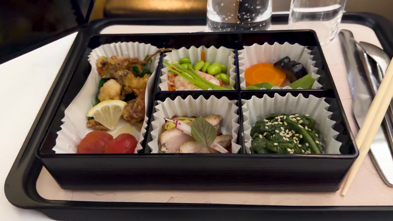 Hand öffnet eine traditionelle japanische Bento-Box-Mahlzeit im Flugzeug