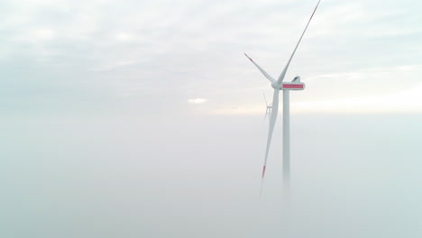 aerial shot of windmill turbines above a layer of dense mist, producing green, clean energy