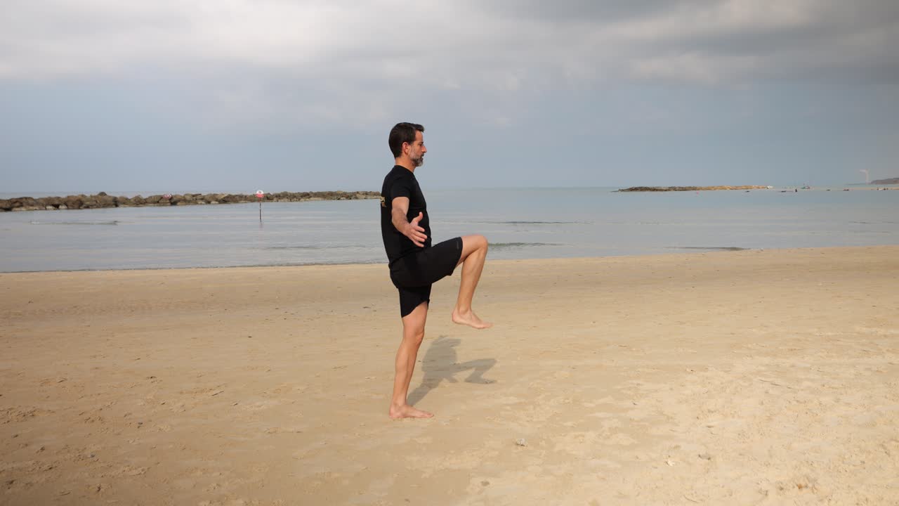 Na pozadí oceánu, zralý muž dělá výpady a cvičí, aby zůstal fit.