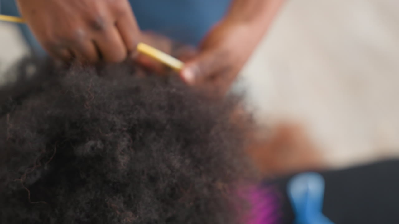 Primo piano di capelli afro che vengono districati con mani delicate, genitore che accudisce che liscia i ricci testurizzati, pettine a denti larghi e separazione con le dita, luce domestica accogliente, routine lenta e paziente per il comfort del cuoio capelluto.