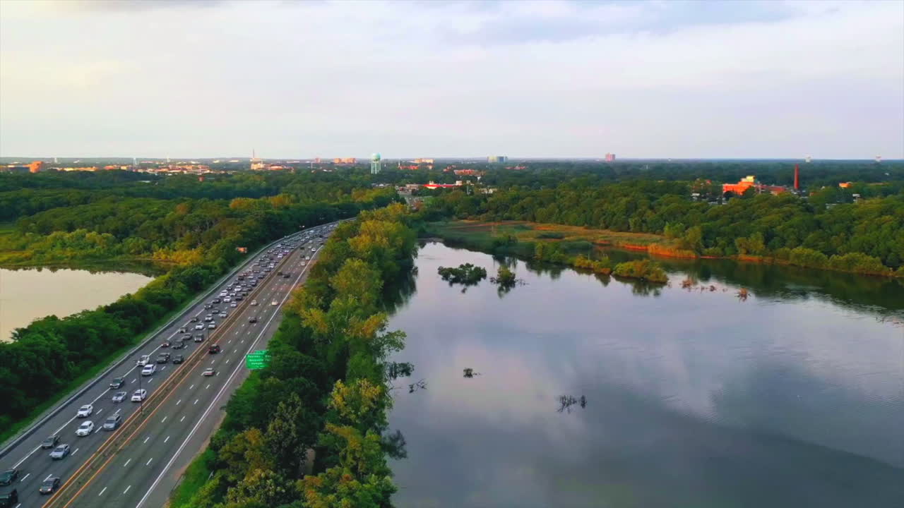 해가 지는 동안 왼쪽 근처 고속도로에서 교통량이 많은 호수 위로 극적인 공중 하이퍼 랩스가 빠져나갑니다.