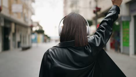 young hispanic woman on back view listening to music at street