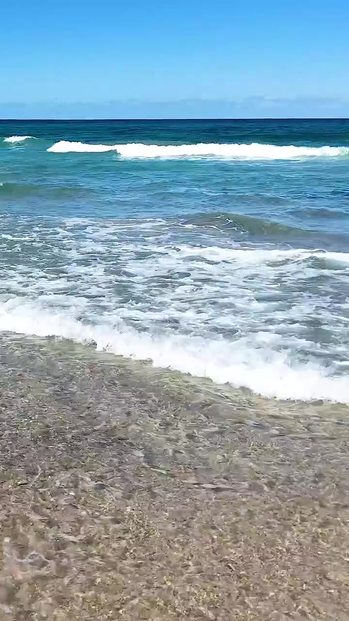 Acqua turchese limpida e schiuma di mare bianca si infrangono su una spiaggia sabbiosa sotto cieli blu.