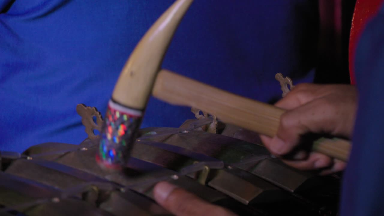 A close-up shot of a gamelan performance in Bali, Indonesia, focusing on the musician's hands and the mallet