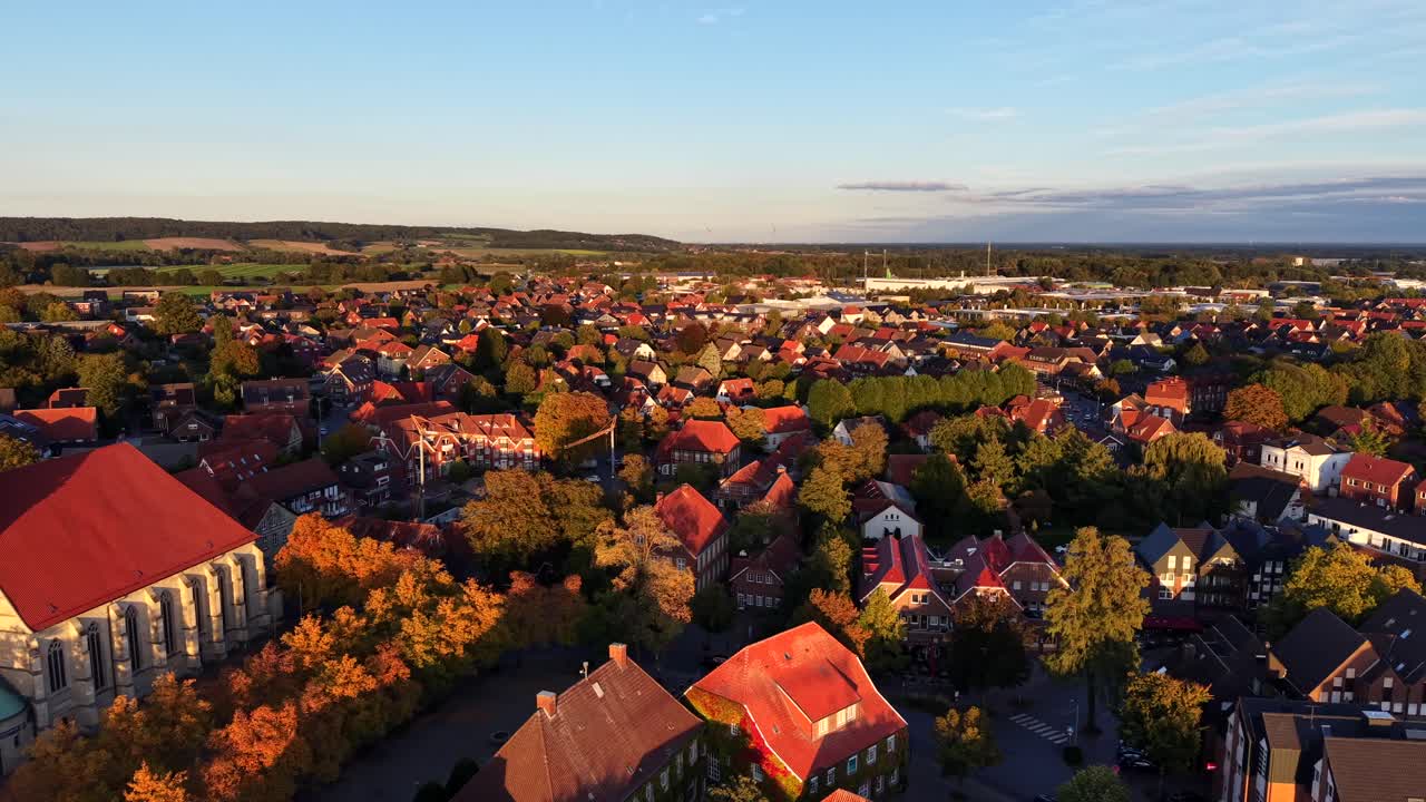 Golden hour in German city with historic buildings, church and red tikes on roof. Colored trees in fall season. Beautiful small town in Europe, rolling hills in distance. Aerial forward wide shot