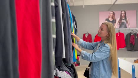 young woman buying used sustainable clothes from second hand charity shop. sale, shopping, fashion and people concept – woman chooses clothes in vintage clothing store. vertical video.