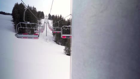 Abandoned-chairlift-in-an-empty-ski-resort,-stopped-cableway-and-ropeway,-ski-slopes-deserted-during-Covid-19-coronavirus-pandemic,-snowy-mountains-in-winter