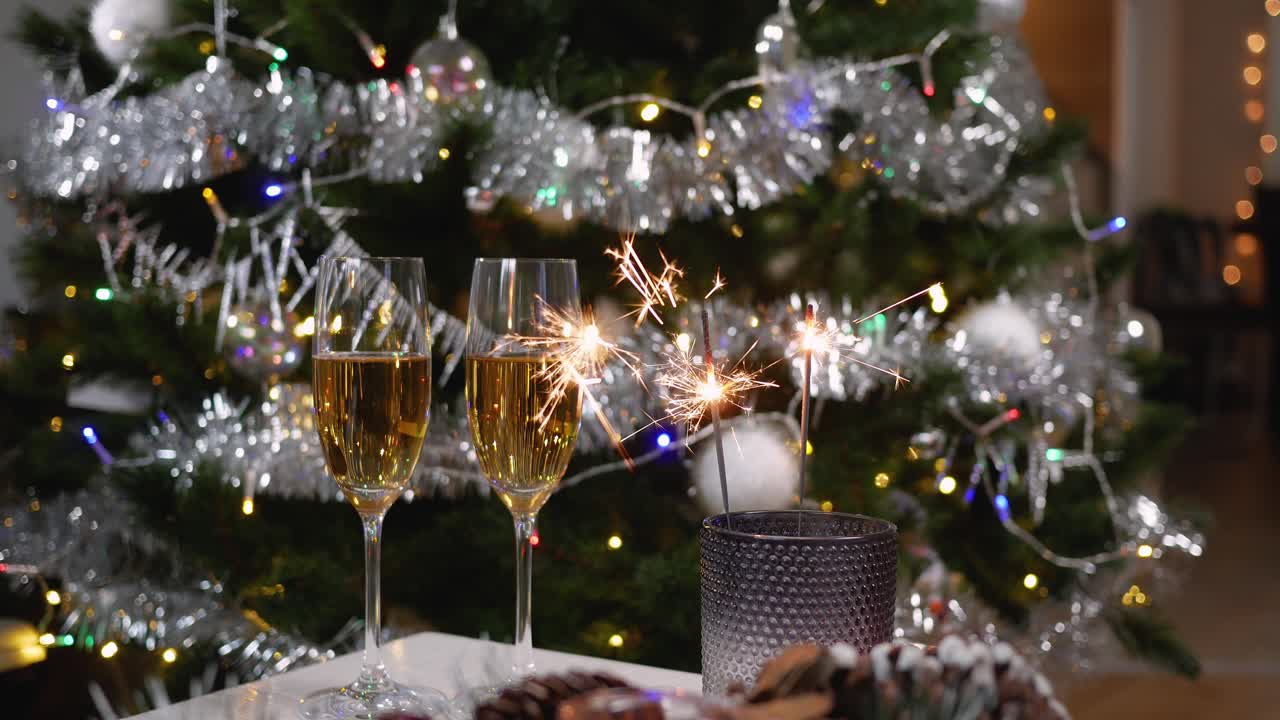 To glas mousserende champagne ved siden af de brændende stjernekastere i en holder på et bord mod baggrunden af et pyntet juletræ.