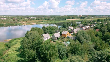 Luftaufnahmen-Von-Landhäusern-Neben-Einem-Ruhigen-Fluss,-Die-Beim-Aufsteigen-Der-Drohne-Eine-Wunderschöne-Spiegelung-Der-Wolken-Im-Wasser-Einfangen