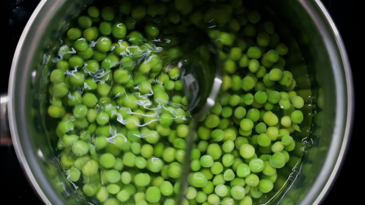 Close up of a spoon picking up green pees with a spoon from a pot with water
