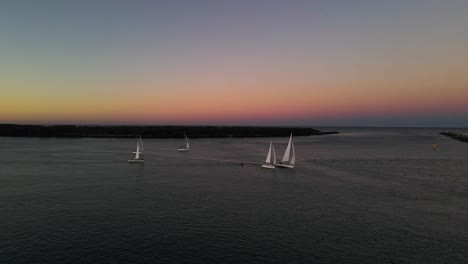 high panning panoramic view of a group of fast moving sailing boats against a colorful sunset backdrop