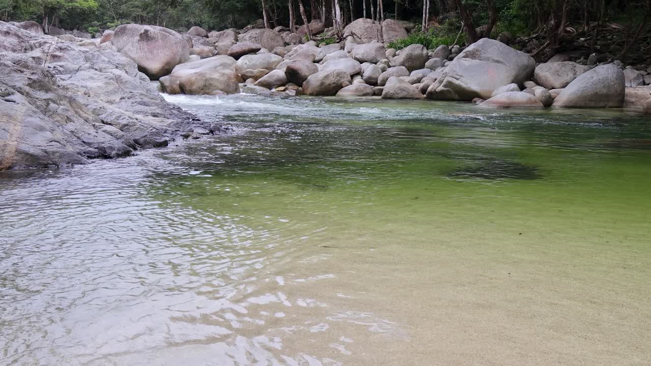 Clear water flows over rocks in a lush rainforest setting, creating a tranquil and natural atmosphere