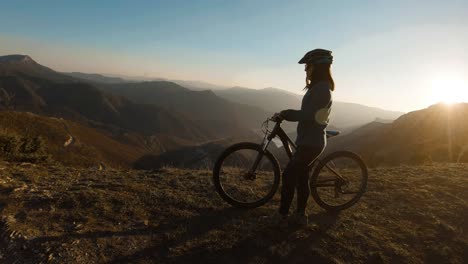 girl pushing bike at the top of a mountain at sunset