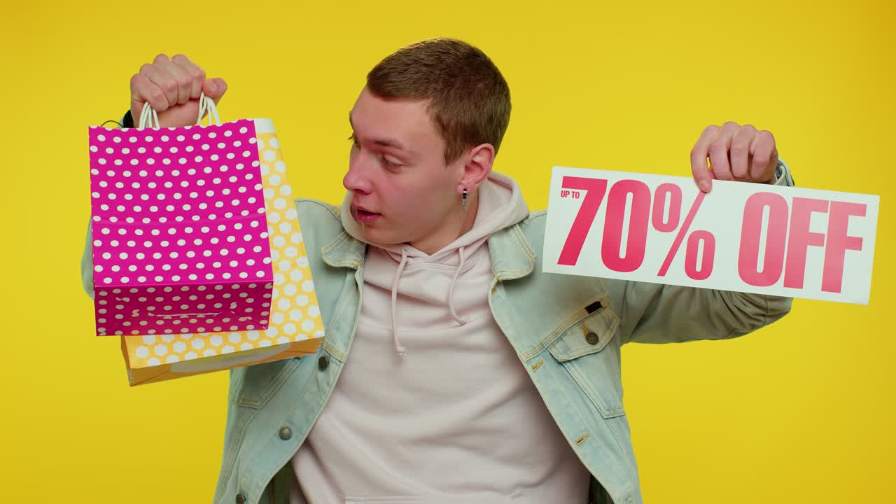 hombre emocionado sosteniendo bolsas de compras y un cartel de 70% de descuento
