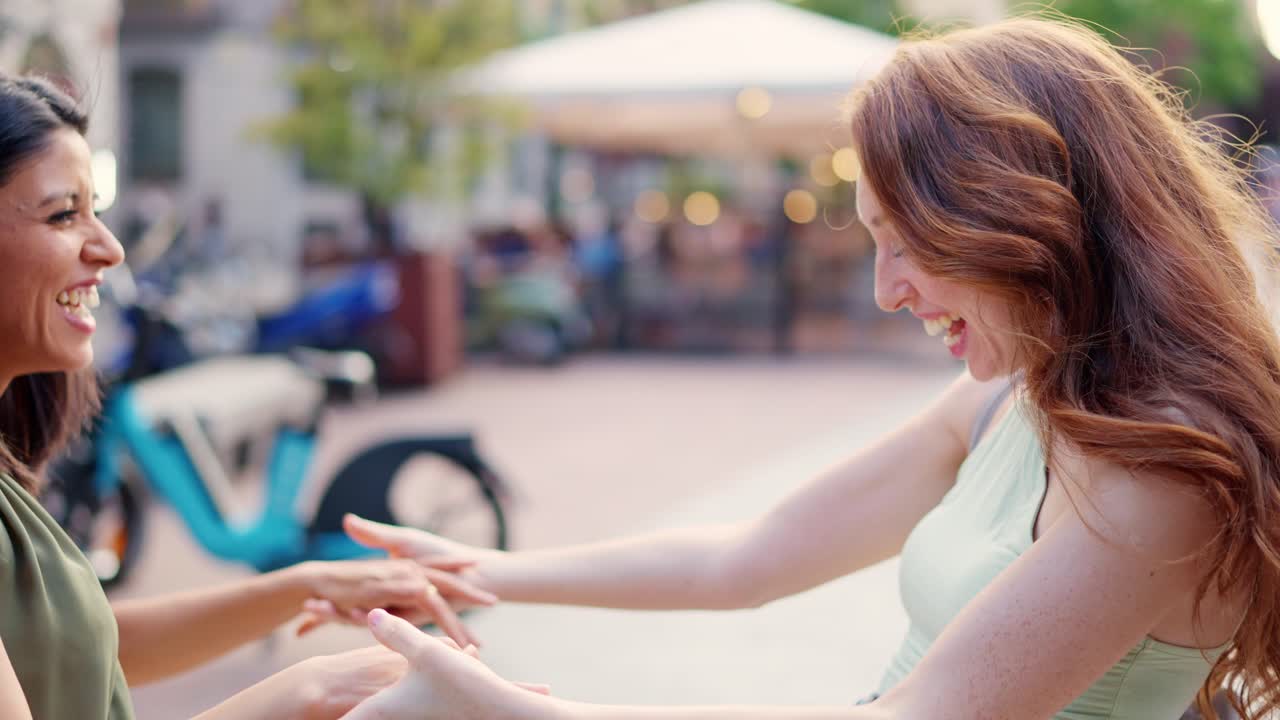 Two happy women friends laughing and holding hands outdoors