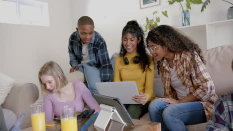 un grupo feliz y diverso de amigos adolescentes sentados en el sofá y usando una computadora portátil en casa, en cámara lenta