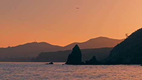 Bunter-Orangefarbener-Sonnenuntergang-Am-Strand-Mit-Der-Silhouette-Von-Fallschirmen,-Die-Im-Hintergrund-Schweben