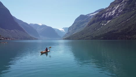 kayaking in spectacular surroundings at lovatnet lake loen nordfjord norway - static aerial with girl kayaking towards camera