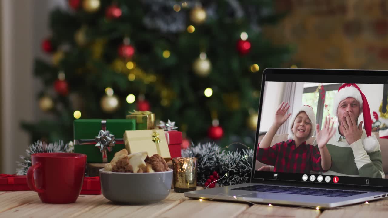 padre y hijo felices saludando en una videollamada en una computadora portátil, con decoraciones de navidad y árbol