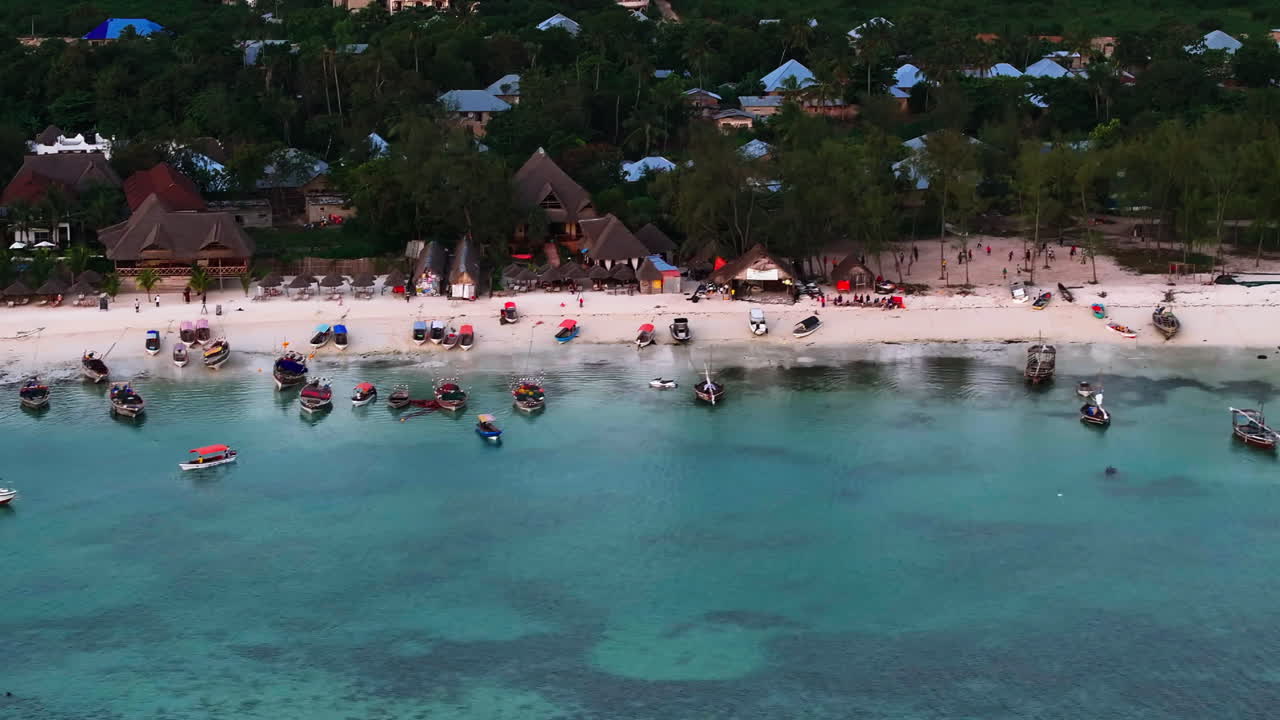 Tanzanya, Zanzibar adasında gün batımında uzun kuyruklu teknelerin bulunduğu, bembeyaz kumsalı ve kristal berraklığındaki suyu drone ile çekilmiş yazlık görüntüsü