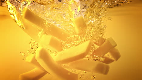 raw french fries falling into hot oil - side view of yellow liquid while potatoes cut into chips break through the surface