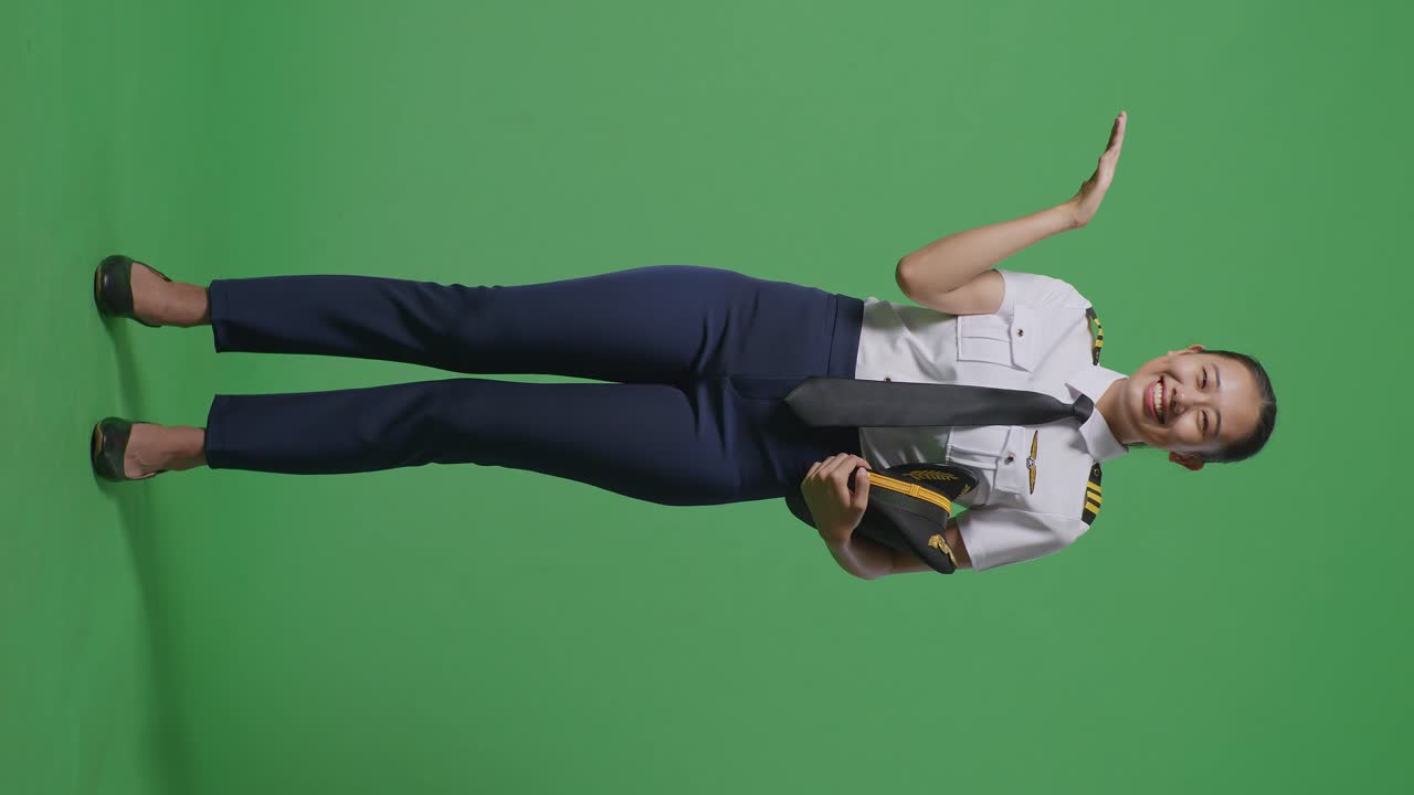 녹색 스크린 배경 스튜디오에 서 있는 동안 웃고 을 가리키는 아시아 여성 조종사의 몸이 가득 차 있습니다.