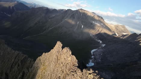 FPV-drone-elegantly-descends-a-mountain-ridge-beside-a-meandering-river,-bathed-in-the-warm-hues-of-a-breathtaking-sunset,-a-mesmerizing-descent