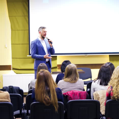 businessman in suit talking to the audience in the conference hall. people listen to the professional lecturer during the business forum indoors.