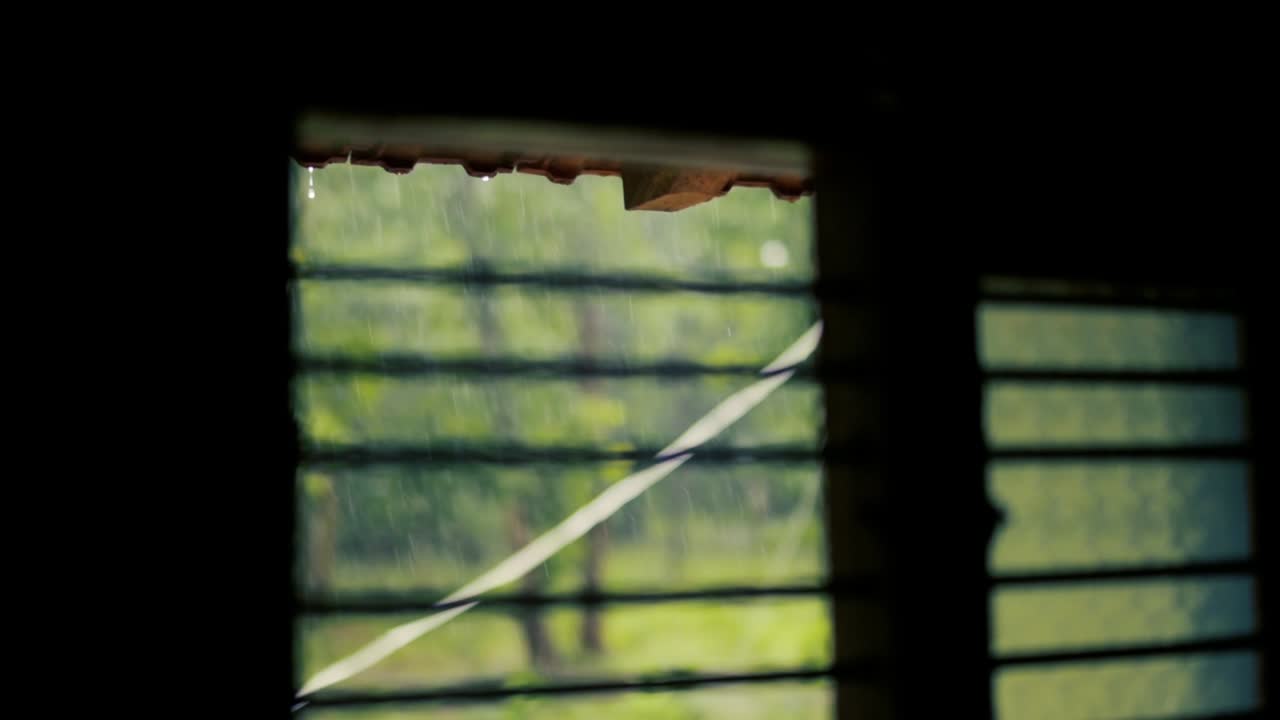 Raindrops dripping from roof seen from window. Static, shallow focus
