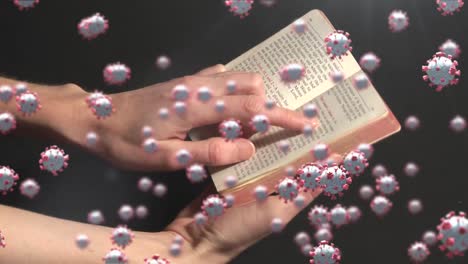 Covid-19-cells-moving-against-hands-holding-a-book