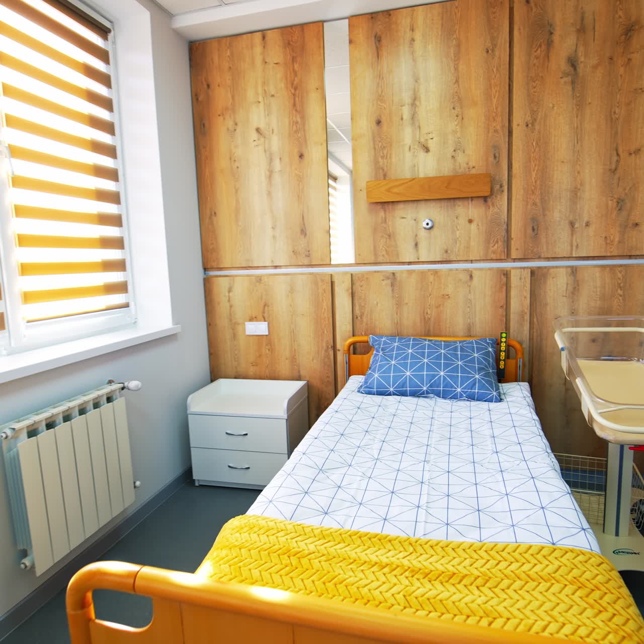 Bright cozy wheeled bed and baby crib beside in a ward of maternity hospital. Modern comfortable room for women after giving birth