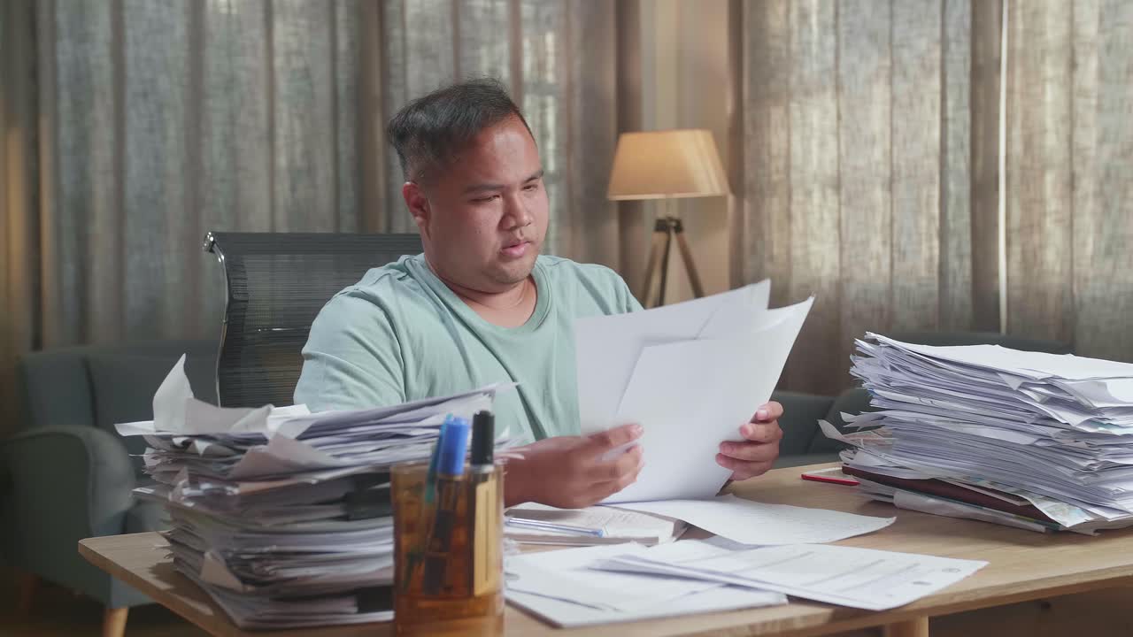 hombre gordo asiático estirándose mientras trabaja duro con documentos en la oficina