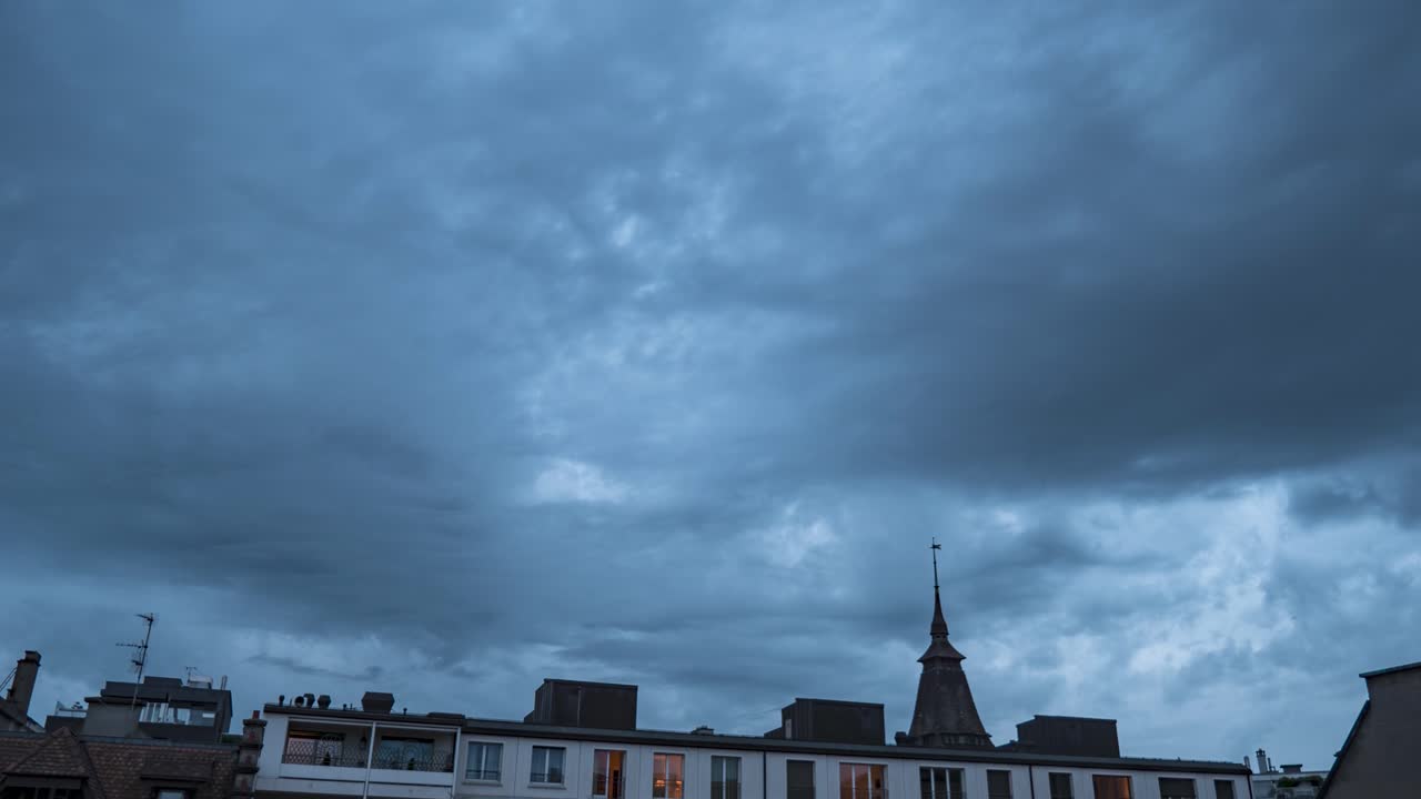 Grey ominous sky and turbulent storm clouds blanket city buildings, time lapse day to night