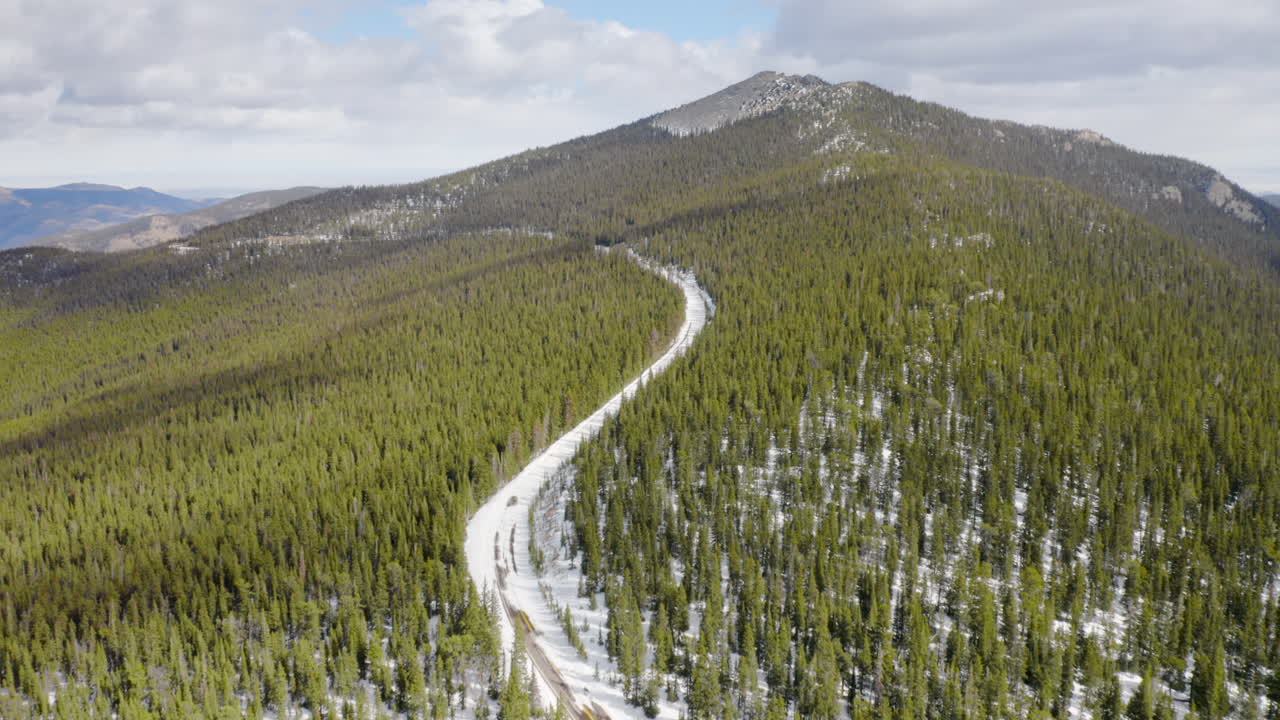 revelación aérea delante de carreteras secundarias soleadas y cubiertas de nieve en las montañas de colorado rodeadas de bosques de pinos verdes brillantes con cielos azules