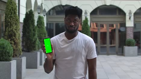 portrait of young african american man is texting message then points to the camera smartphone with green screen and chroma key. gadgets and modern people concept. slow motion. close up