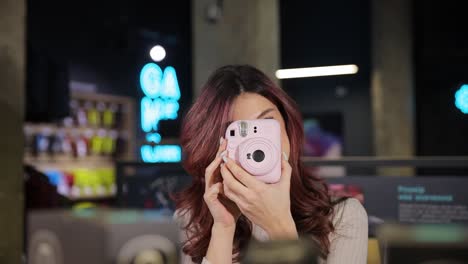 happy woman taking photos with a pink polaroid camera in a hardware store . happy woman taking photos with a pink polaroid camera in a hardware store