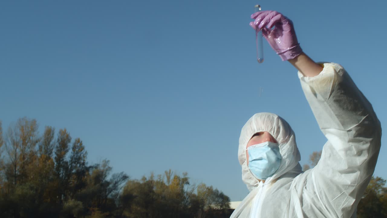 muestreo de agua del río al tubo de ensayo, mujer con traje protector, plano medio