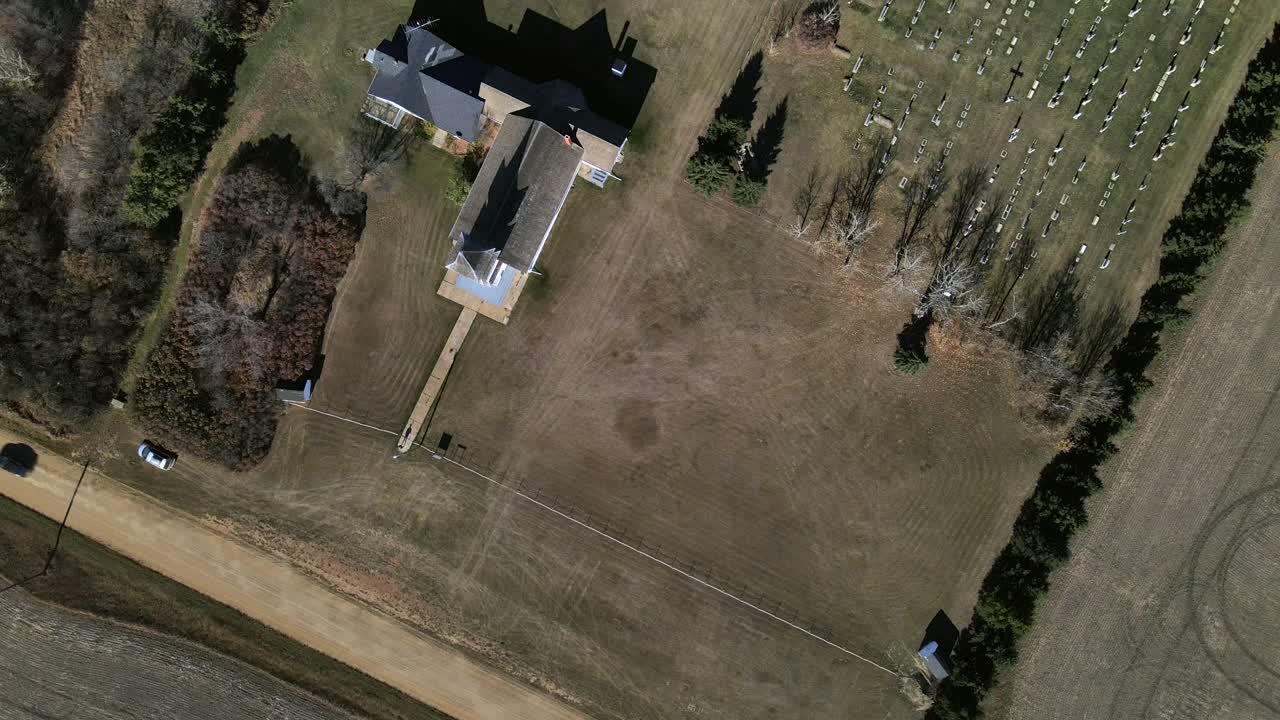 앨버타주 플래그스태프 카운티에 있는 먼지투성이 흙길을 따라 운전하고 세인트 보니페이스 교회를 지나가는 검은색 자동차를 보여주는 높은 곳에서 하향식 공중 전망