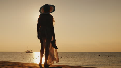 A-Stylish-Girl-In-Fluttering-Clothes-And-A-Broad-Brimmed-Hat-Meets-The-Sunrise-On-A-Sea-Pier