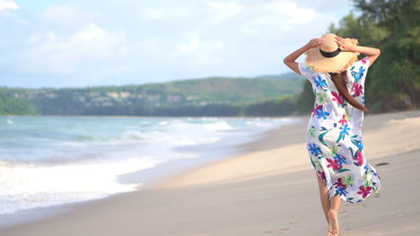 Rückansicht-Einer-Eleganten-Frau-Mit-Hut-Und-Geblümtem-Kleid,-Die-Am-Strand-Spazieren-Geht