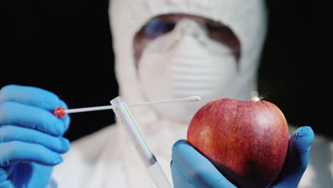 a man in protective clothing and gloves takes a smear from a large apple