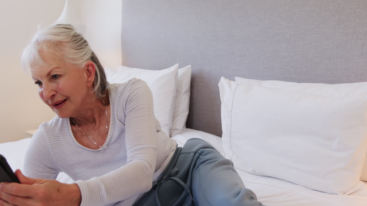 Senior woman relaxing on bed, using tablet for reading at home