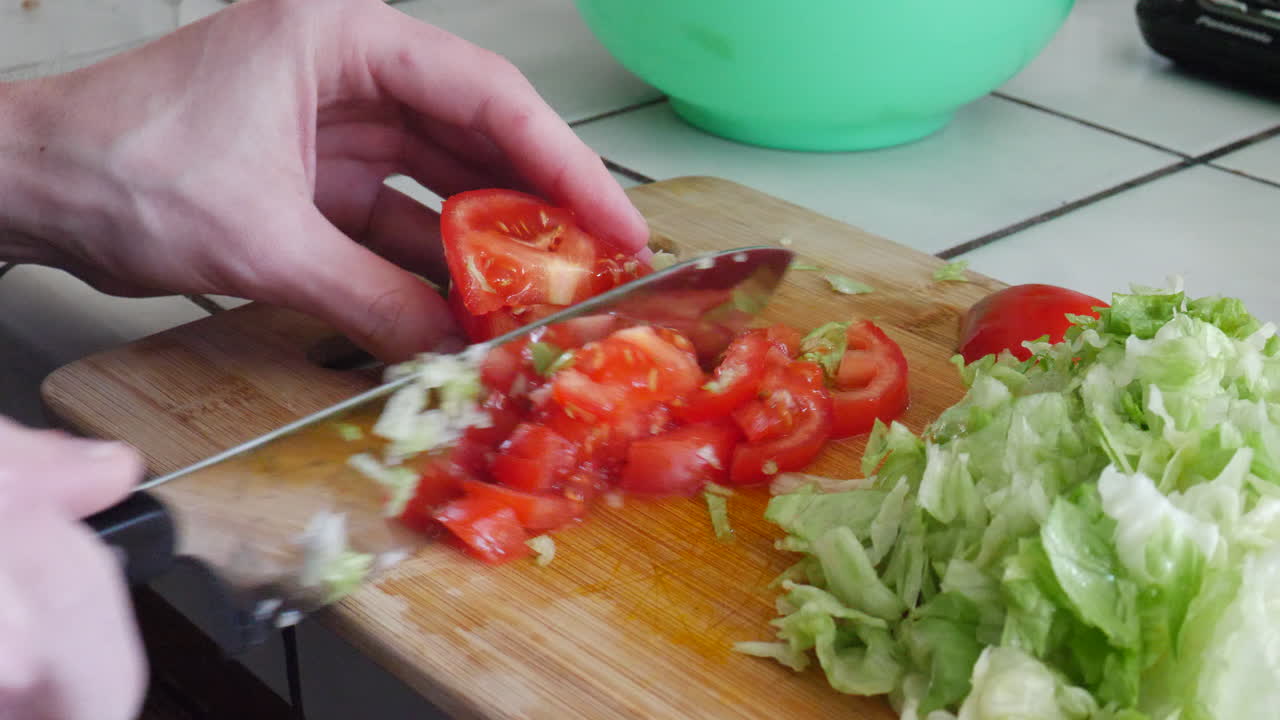 Close up on hands slicing tomatoes and cutting lettuce with a kitchen knife while preparing a healthy vegan meal