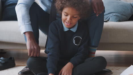 close up of mixed race pre teen boy in school uniform sitting on the floor at home doing his homework helped by his father, sitting behind him on sofa, tilt shot