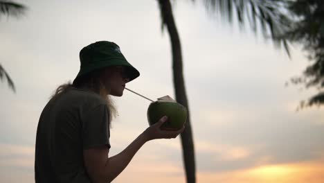 women enjoying a fresh coconut at a beach under some palm trees, low angle shot