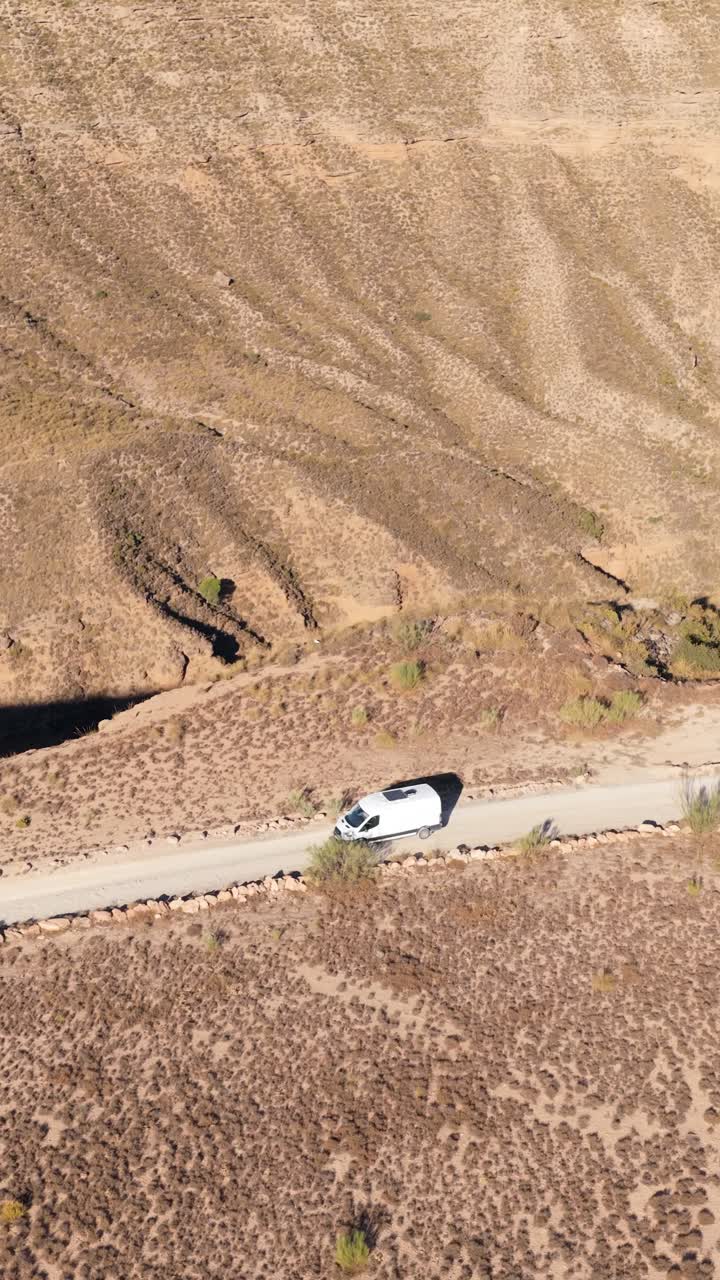 Vista Aerea di un Camper Bianco che Percorre una Strada Sterrata Attraverso Montagne Aride