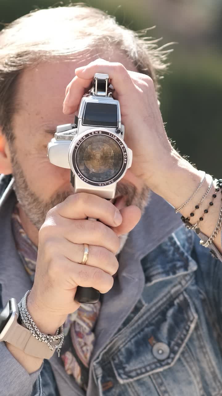 Mature man shooting video in city park with vintage camera. Vertical footage