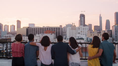 rear view of friends gathered on rooftop terrace looking out over city skyline